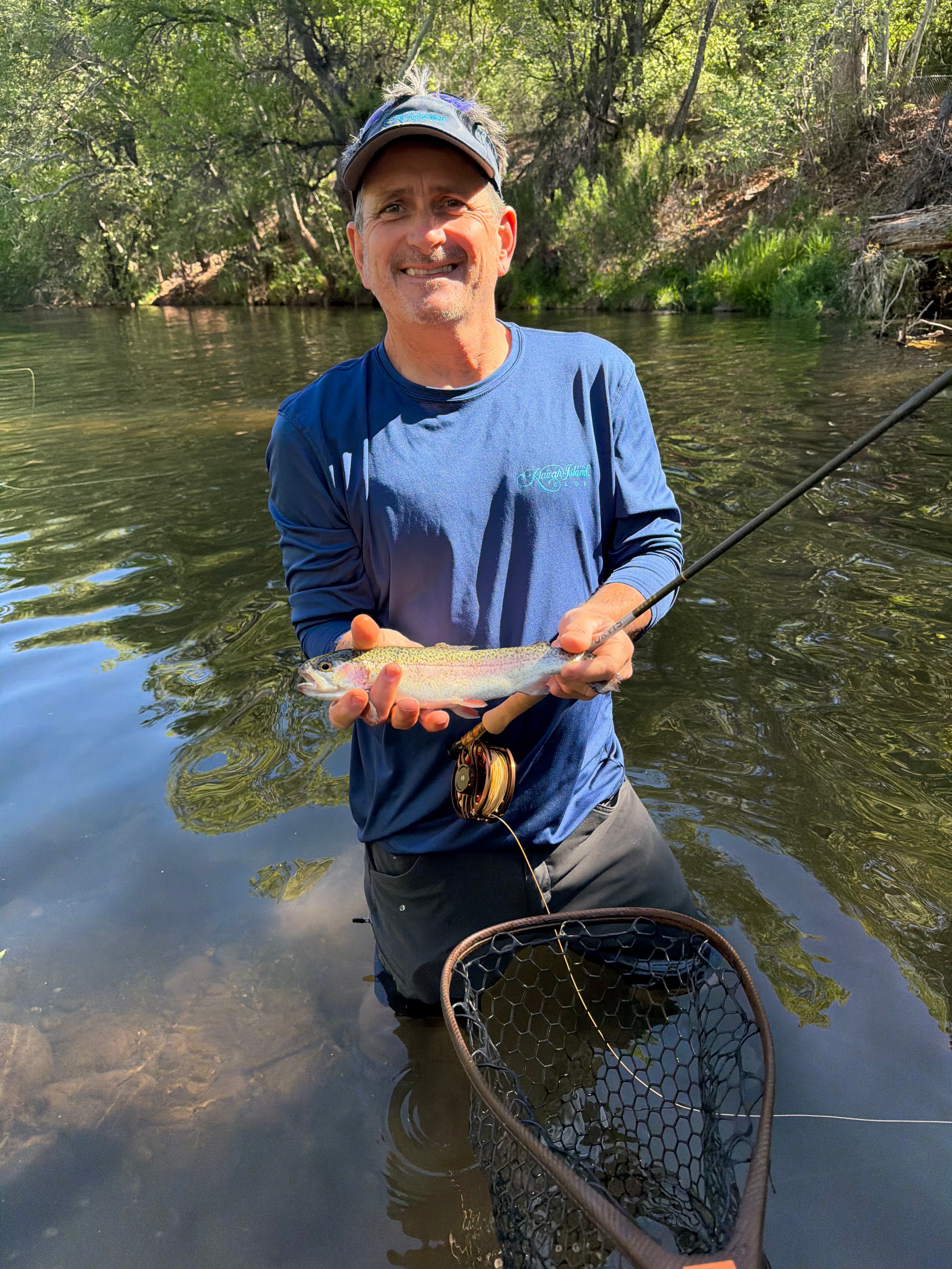 Smiling angler holding a rainbow trout streamside with net