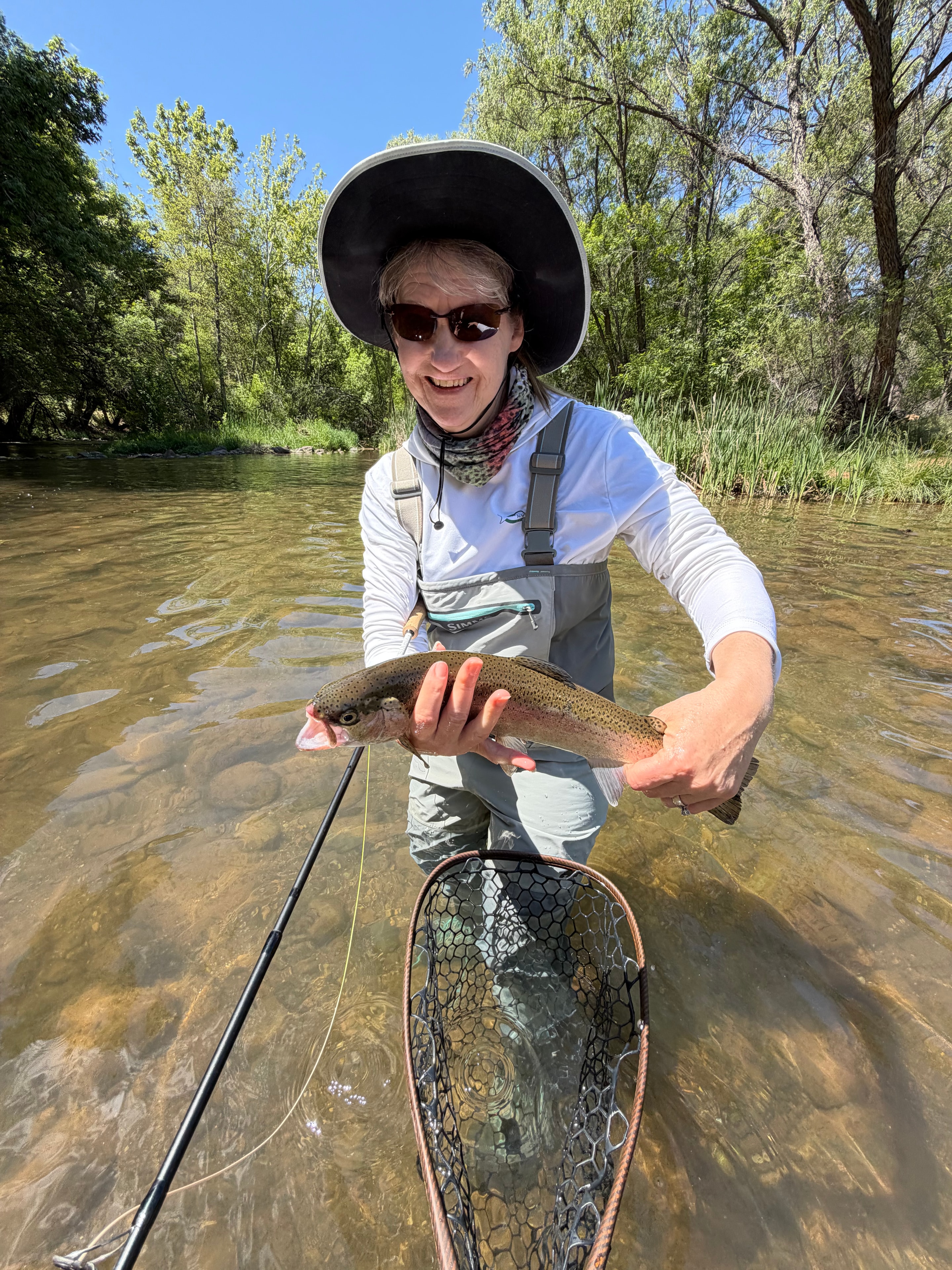 Female angler holding a rainbow trout while wading a clear stream