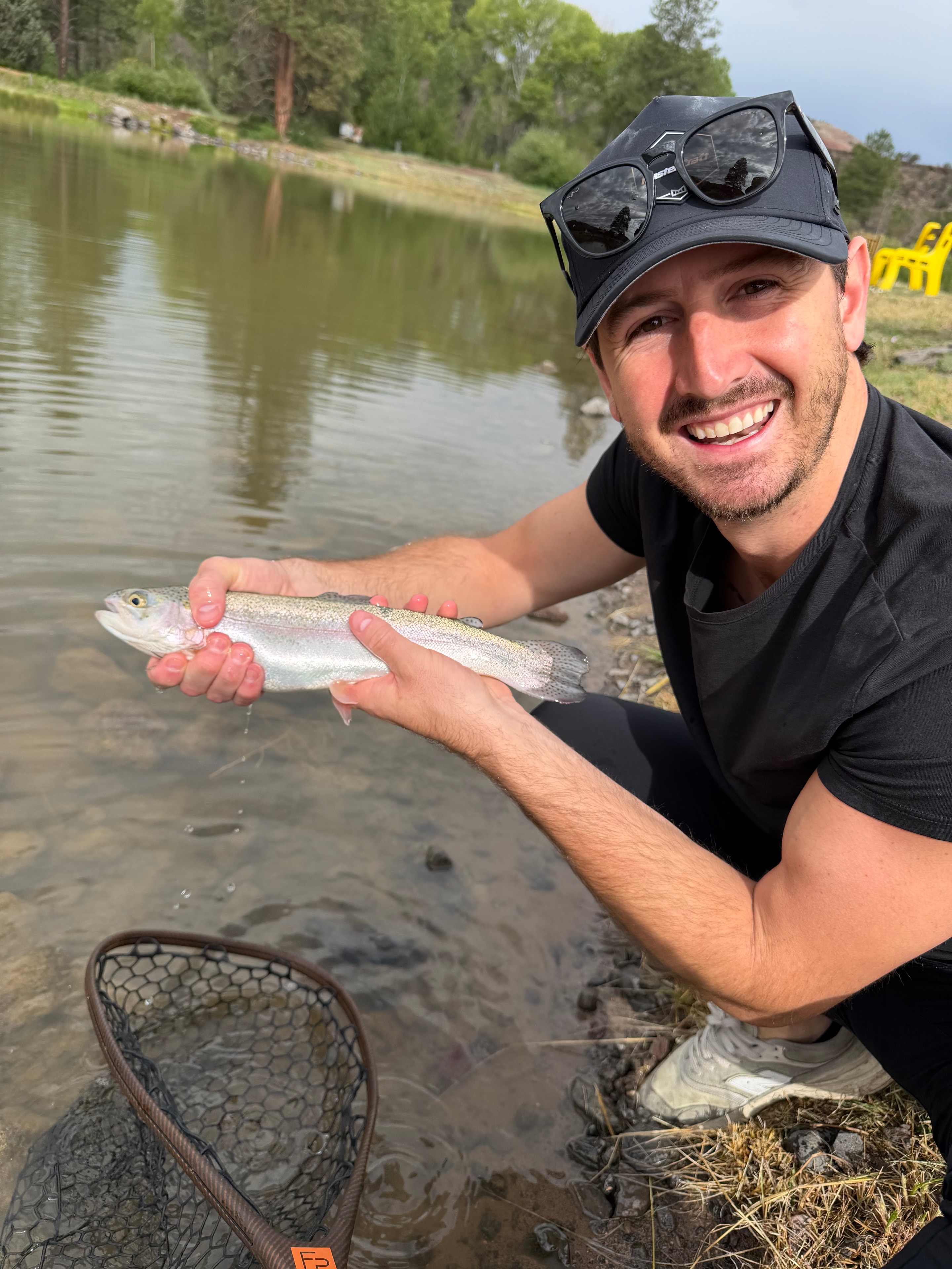 Young angler smiling with a rainbow trout at the water's edge